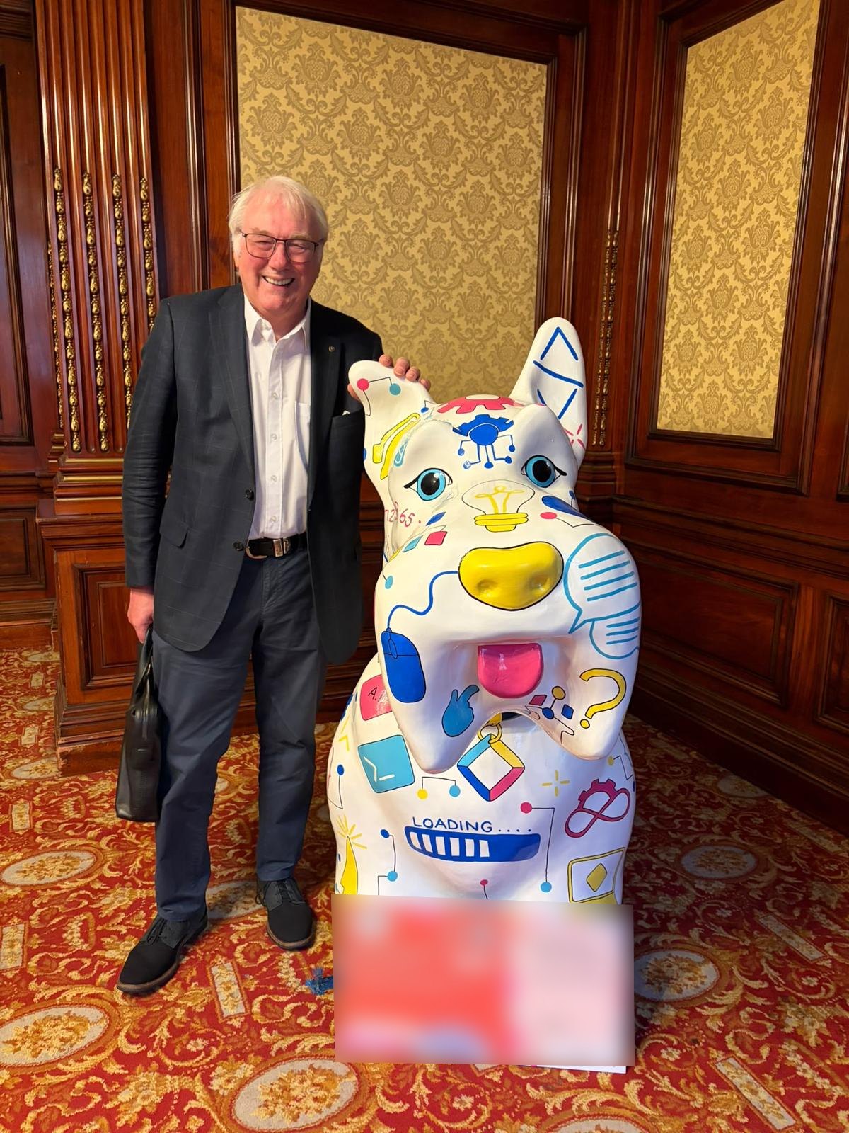 Barry Wood smiling beside a white Scottie dog sculpture covered in colourful software-themed drawings, with its information board in front.